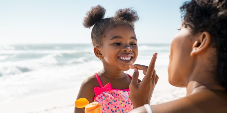 Black mother putting sunscreen on daughter at the beach